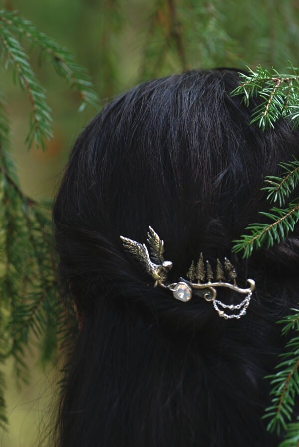 Woman wearing a silver owl hair comb with pine tree details, styled in dark hair among forest branches.