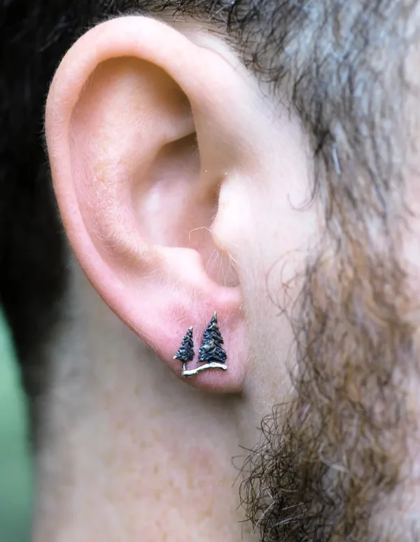 Silver pine tree stud earrings worn on a man's ear, symbolizing strength and nature.