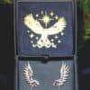 Silver owl earrings with opal glass drops displayed in an elegant jewelry box with golden owl emblem.