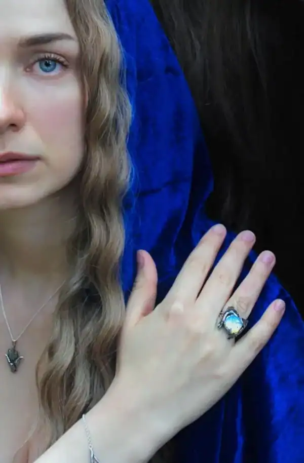 Woman in blue cloak wearing owl silver ring with glowing opal stone.