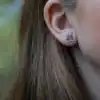 Minimalist silver pine tree earrings worn on a woman's ear, inspired by Nordic forests.