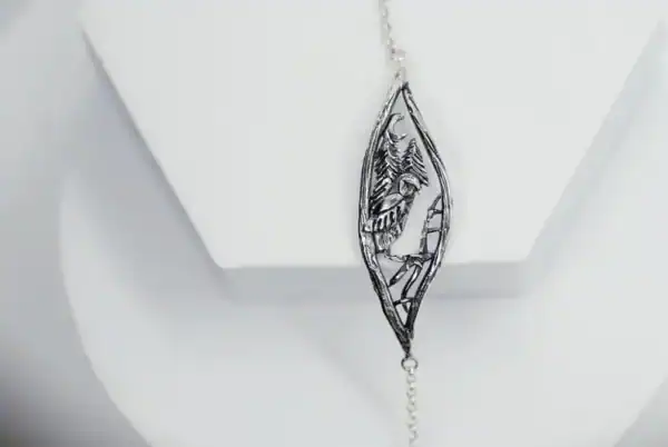 Studio shot of "Nattuggla" silver bracelet showing owl and pine trees.
