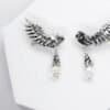 Close-up of handcrafted silver owl wing earrings with opal glass drops on white background.