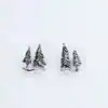 Detailed shot of silver pine tree stud earrings lying flat on a white surface.