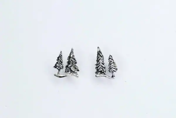 Detailed shot of silver pine tree stud earrings lying flat on a white surface.