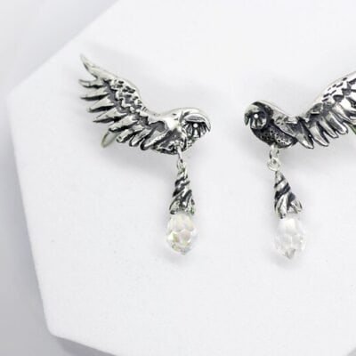 Close-up of handcrafted silver owl wing earrings with opal glass drops on white background.
