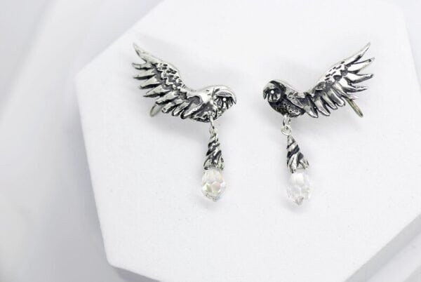 Close-up of handcrafted silver owl wing earrings with opal glass drops on white background.