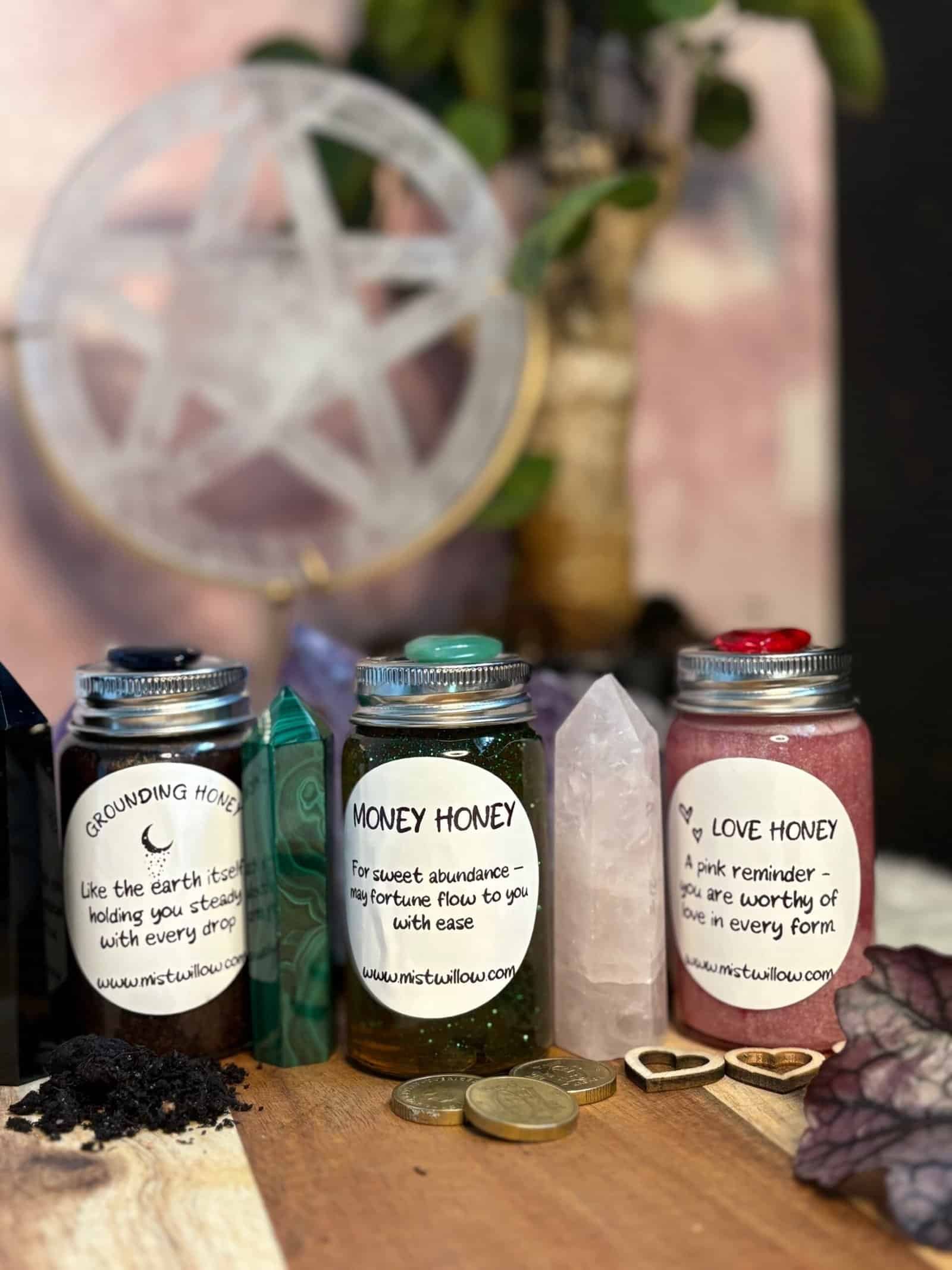 Three jars of Mistwillow’s Intentions Honey – Grounding Honey, Money Honey, and Love Honey – displayed with crystals, coins, and pentacle for ritual magic.