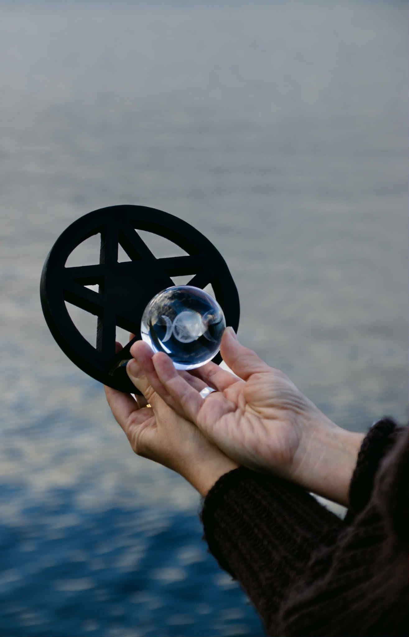 Hand holding black obsidian pentagram for witchcraft ritual near water