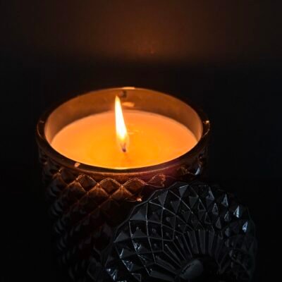 Black grimoire ritual candle with flame in textured glass jar on dark background